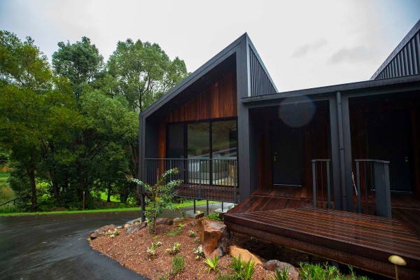 An eco lodge in a lush green setting shot in rainy weather with timber decking and feature walls and dark grey steel Sharpline roof and wall cladding